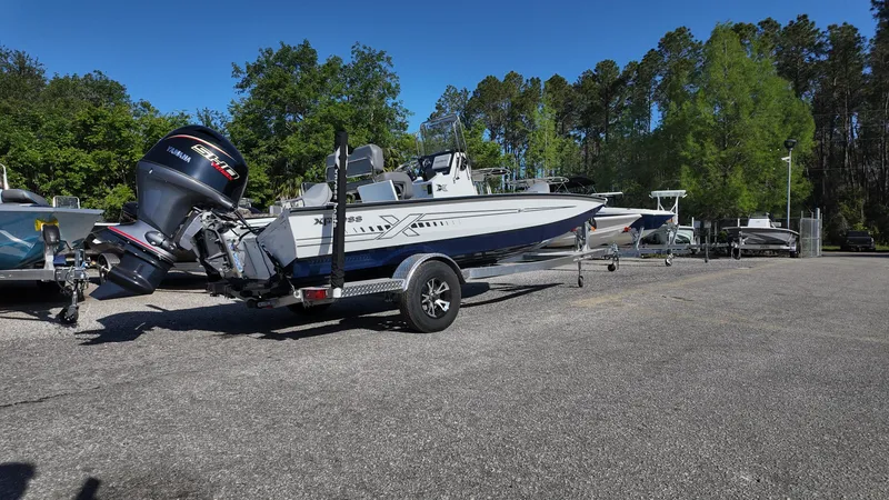 Slide: The Image of 2025 Xpress H20B boat on trailer in parking lot, surrounded by trees. - 18