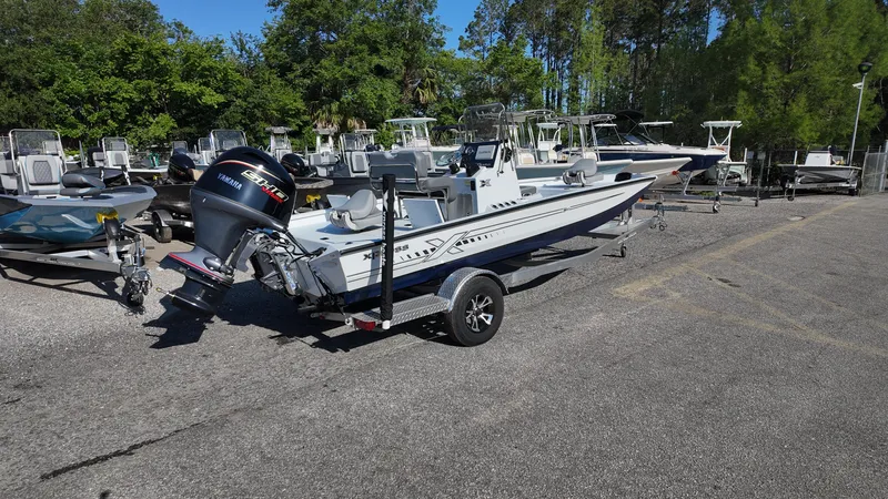 Slide: The Image of 2025 Xpress H20B boat on trailer in outdoor lot with trees in background. - 19