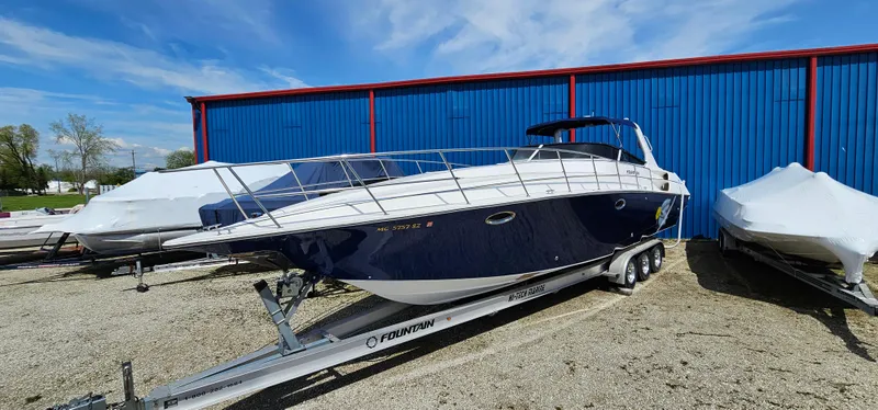 Slide: The Image of 2002 Fountain 38 Express Cruiser on trailer, parked outdoors near blue building. - 0