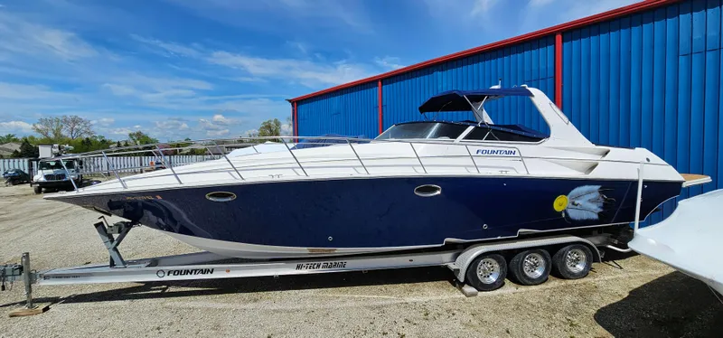 Slide: The Image of 2002 Fountain 38 Express Cruiser on trailer, parked outdoors near blue building. - 1