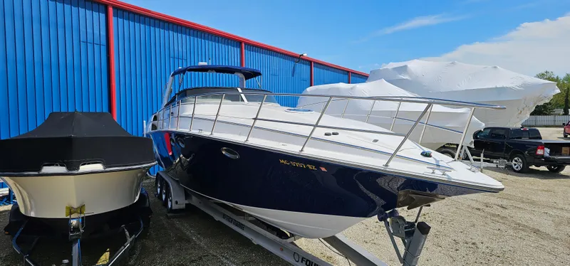 Slide: The Image of 2002 Fountain 38 Express Cruiser boat on trailer, parked near blue and red building. - 2