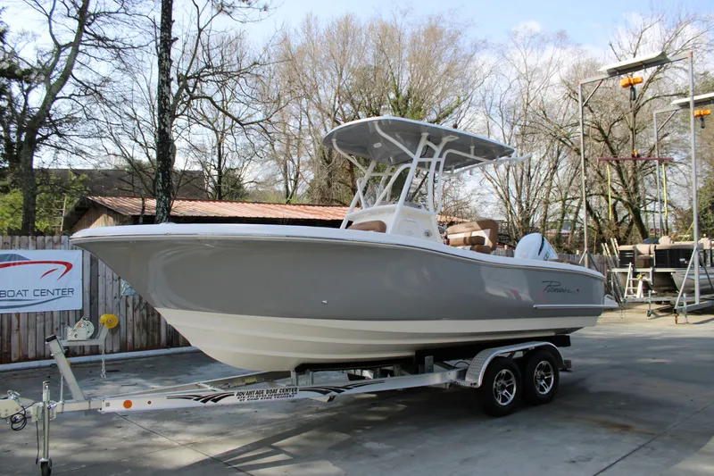 Slide: The Image of 2025 Pioneer 222 Islander boat on trailer, parked outdoors near trees and a building. - 2