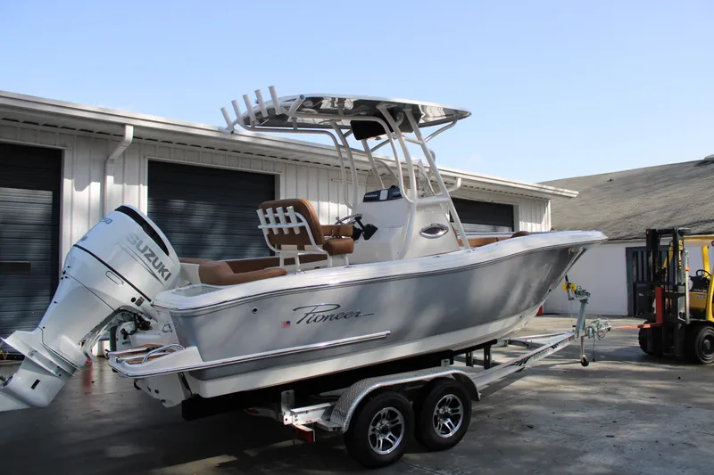Slide: The Image of 2025 Pioneer 222 Islander boat on trailer with Suzuki outboard motor, parked near warehouse. - 3
