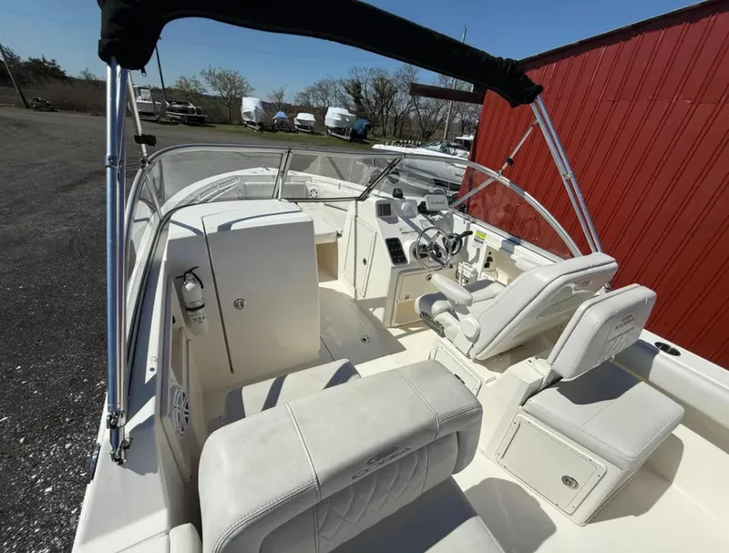 Slide: The Image of 2021 Cobia 220 Dual Console boat interior with seating and steering wheel, docked near a red building. - 11