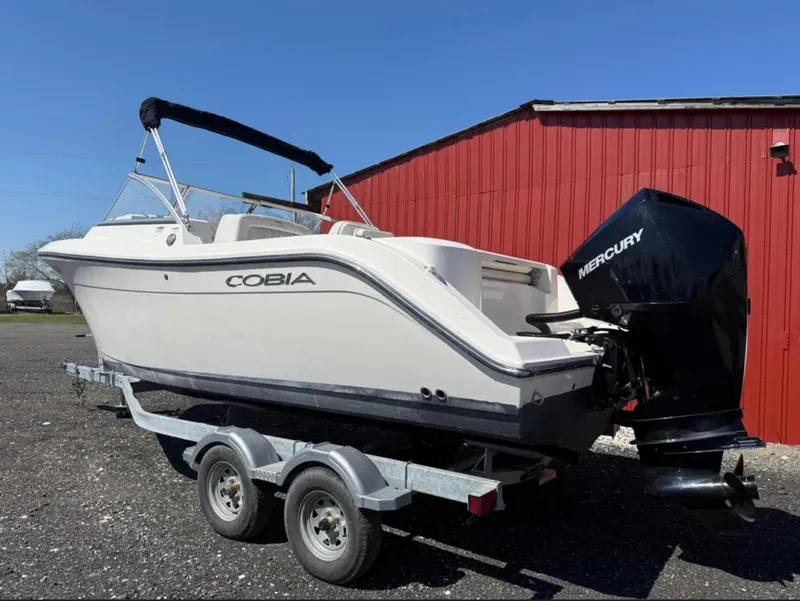 Slide: The Image of 2021 Cobia 220 Dual Console boat on trailer, with Mercury outboard, near red building. - 3