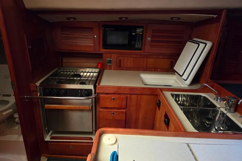Slide: The Image of 2000 J Boats J/46 yacht kitchen with stove, sink, and microwave in wooden cabinetry. - 53