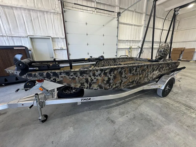 Slide: The Image of 2025 Thor TIMBER HAMMER boat with camouflage design on a trailer in a garage. - 1