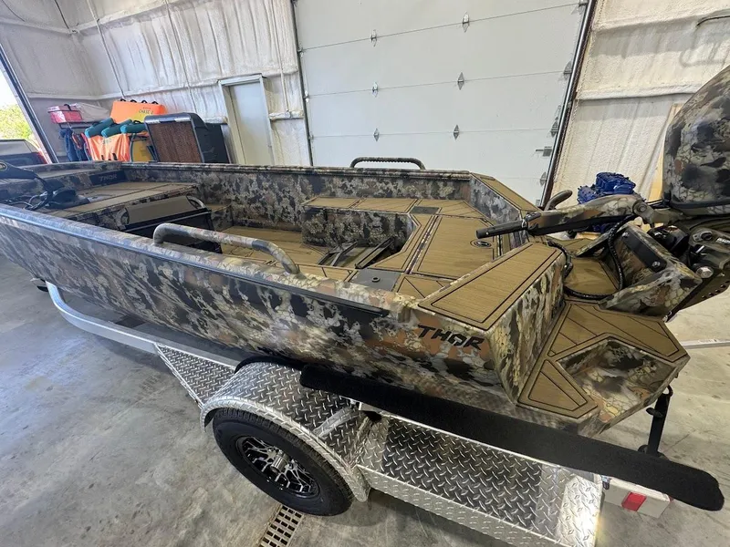 Slide: The Image of 2025 Thor TIMBER HAMMER boat with camouflage design on a trailer in a garage. - 3