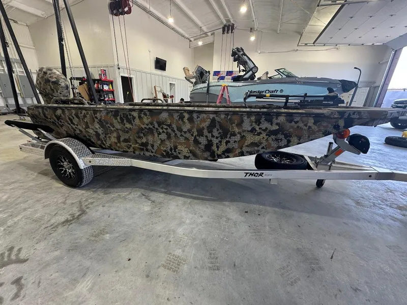 Slide: The Image of Camouflage-patterned Thor TIMBER HAMMER boat on trailer in a spacious garage, 2025 model. - 5