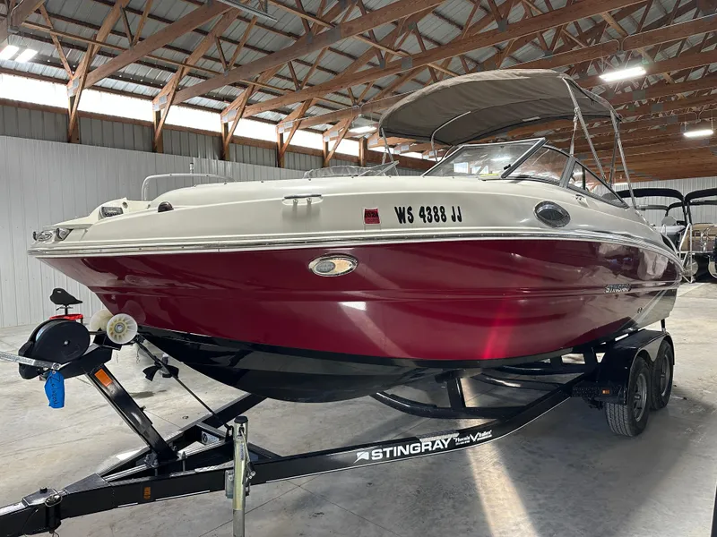 Slide: The Image of 2015 Stingray 215 LR boat with red hull on trailer in a warehouse. - 1