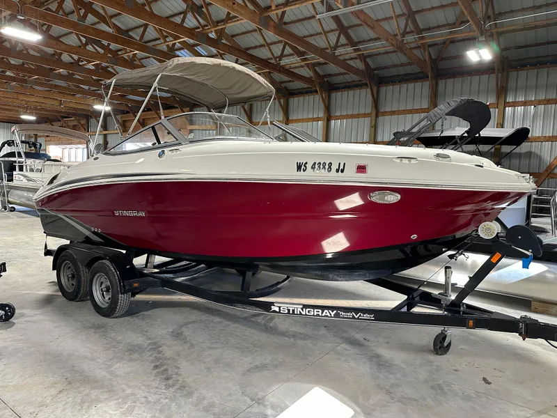 Slide: The Image of 2015 Stingray 215 LR boat with red hull on trailer in a warehouse. - 2