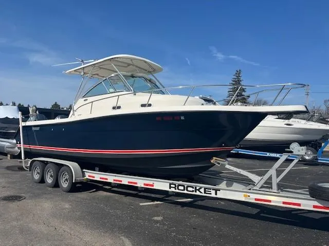 Slide: The Image of 2003 Pursuit 2870 Walkaround boat on a trailer, parked outdoors under a clear blue sky. - 1