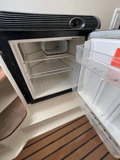 Slide: The Image of 2003 Pursuit 2870 Walkaround boat refrigerator, open and empty, with wooden flooring. - 16