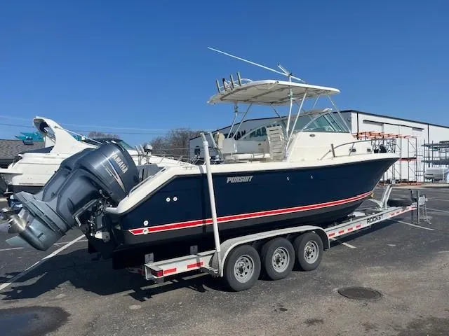 Slide: The Image of 2003 Pursuit 2870 Walkaround boat on trailer with dual outboard engines, parked outdoors. - 2