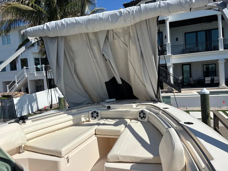 Slide: The Image of 2024 Grady-White Canyon 336 boat with beige seating and canopy, docked near waterfront homes. - 14