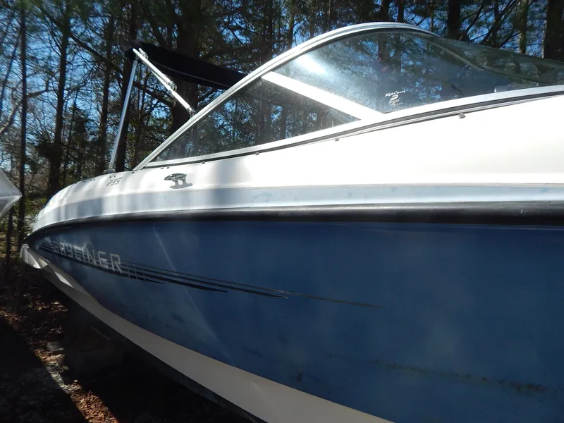 Slide: The Image of 2013 Bayliner 235 Bowrider boat, blue and white, parked outdoors among trees. - 3