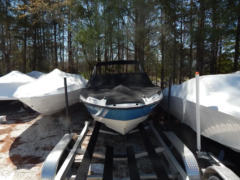 Slide: The Image of 2013 Bayliner 235 Bowrider boat on trailer, covered, surrounded by trees. - 31