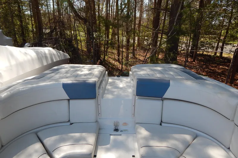 Slide: The Image of 2013 Bayliner 235 Bowrider interior with white and blue seating, surrounded by trees. - 33