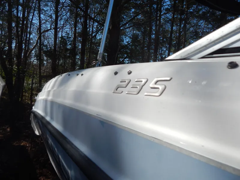 Slide: The Image of 2013 Bayliner 235 Bowrider boat side view with trees in the background. - 4