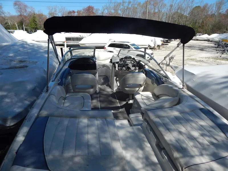 Slide: The Image of 2013 Bayliner 235 Bowrider boat with canopy, parked outdoors, featuring spacious seating and steering console. - 9