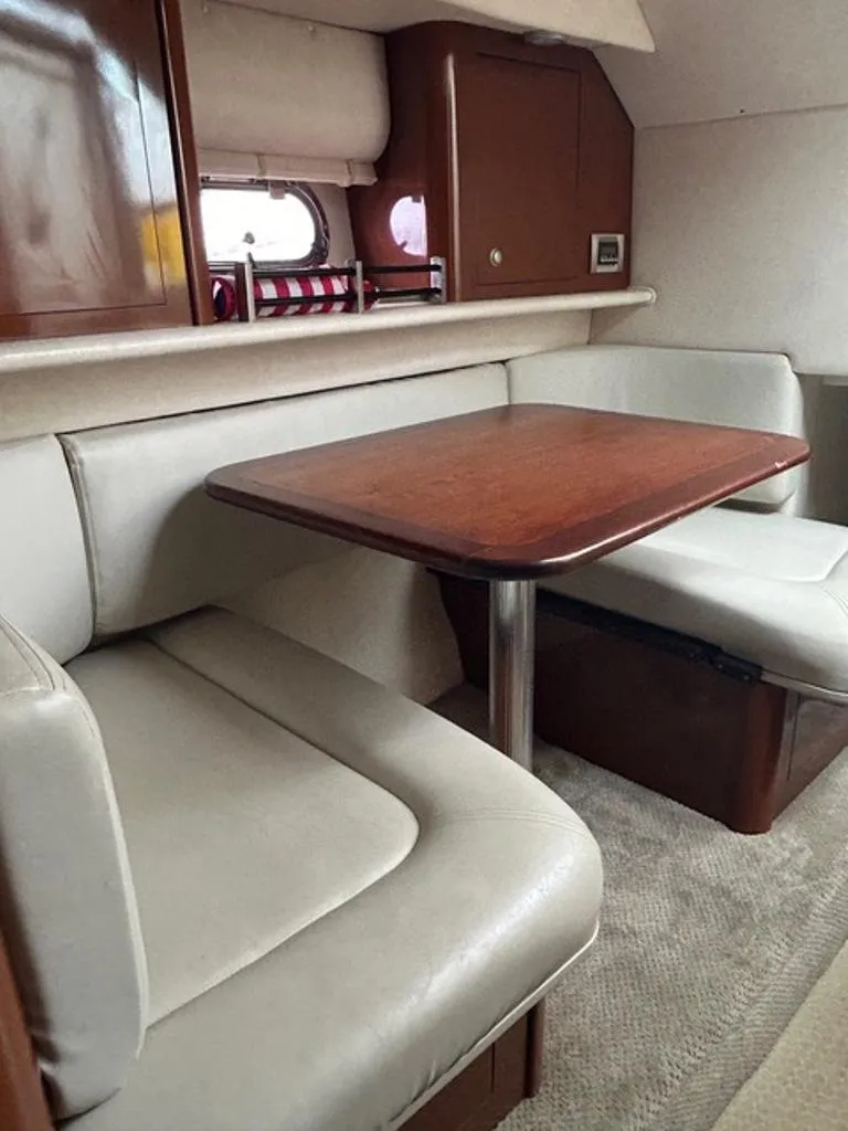 Slide: The Image of 2008 Sea Ray 290 Amberjack cabin with dining area, featuring cushioned seating and wooden table. - 9