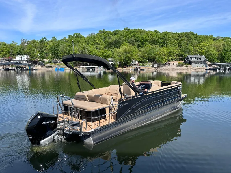 Slide: The Image of 2019 Harris Solstice 240 pontoon boat on a serene lake with lush green shoreline. - 2