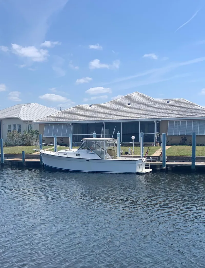 Slide: The Image of 1987 Luhrs Alura 30 boat docked by waterfront home under clear blue sky. - 1