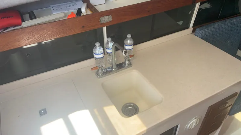 Slide: The Image of 1987 Luhrs Alura 30 boat interior with sink and countertop, featuring water bottles and faucet. - 14