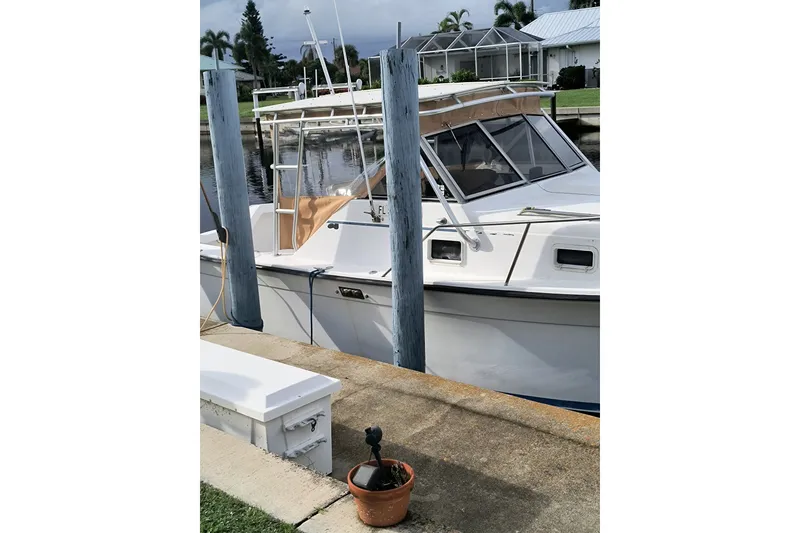 Slide: The Image of 1987 Luhrs Alura 30 boat docked by a waterfront, with a potted plant nearby. - 2