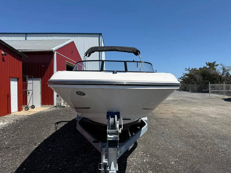 Slide: The Image of 2022 Bayliner VR6 Bowrider OB on trailer, parked near red building under clear blue sky. - 8