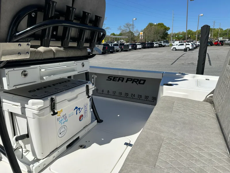 Slide: The Image of 2022 Sea Pro 248 DLX boat interior with seating and cooler, parked outdoors. - 14