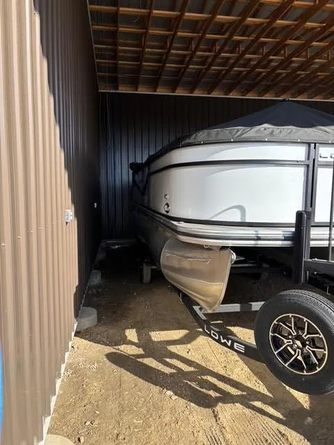 Slide: The Image of 2025 Lowe LS210 boat stored under a metal roof, partially covered, on a trailer. - 3