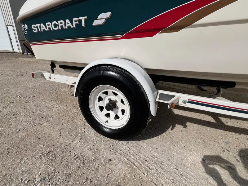 Slide: The Image of 1997 Starcraft 1810 boat trailer with white wheel on gravel surface. - 18