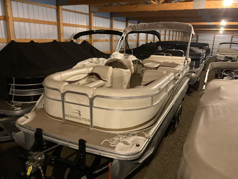 Slide: The Image of 2003 Bennington 2275RL pontoon boat stored indoors, featuring beige seating and protective cover. - 0