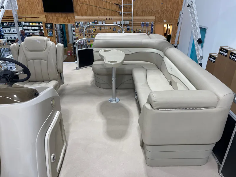 Slide: The Image of 2016 Bennington 22SX boat interior with beige seating and table, displayed in a showroom. - 13