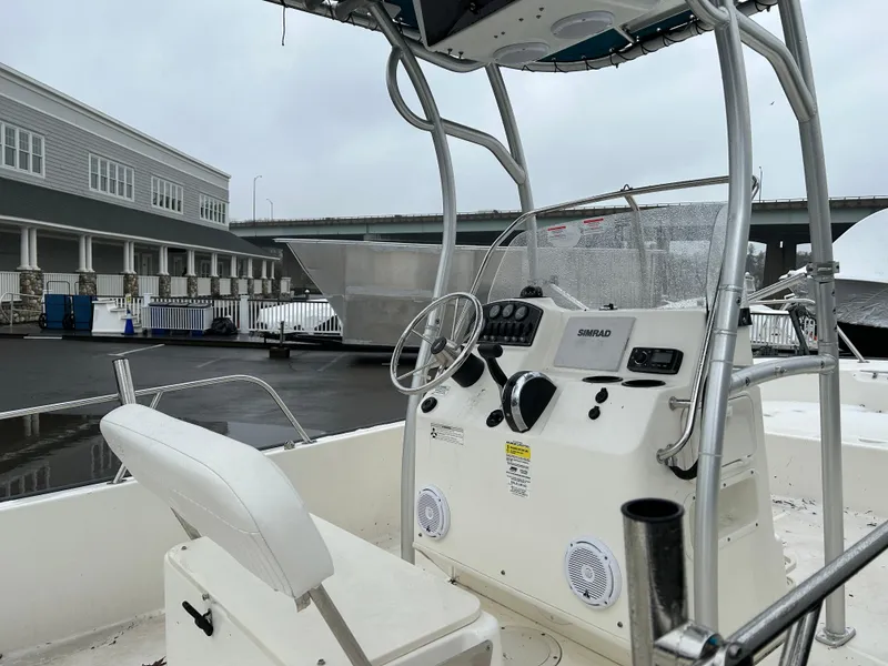Slide: The Image of 2015 Boston Whaler 190 Montauk boat interior with steering console and seating, docked outdoors. - 4