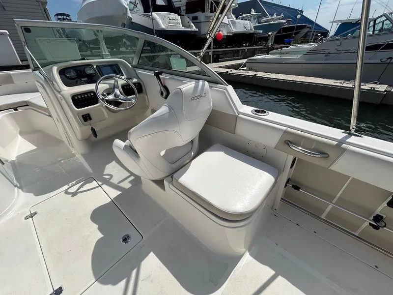 Slide: The Image of 2014 Robalo R227 boat interior with helm, white seating, and docked yachts in background. - 19