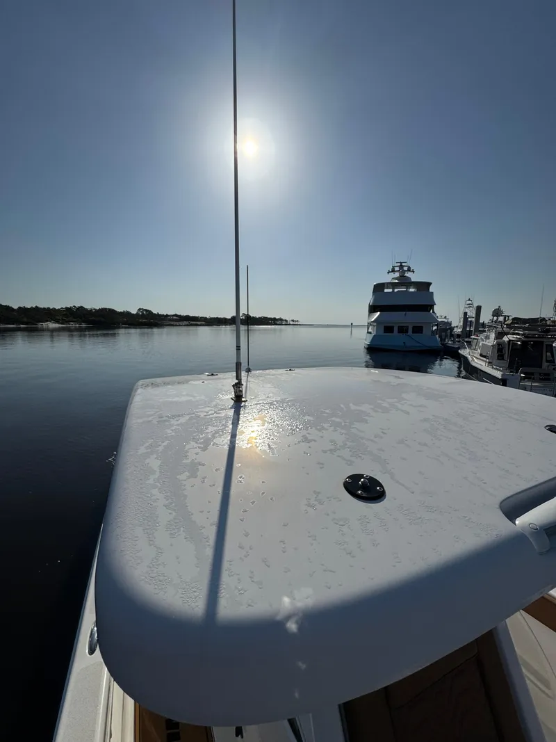 Slide: The Image of 2023 Twin Vee 280 GFX CC boat on calm water at sunrise, docked near other vessels. - 46