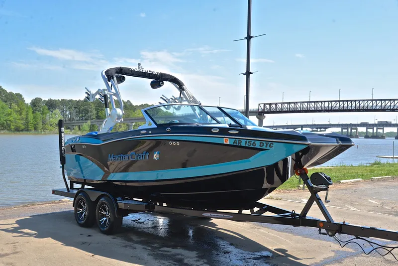 Slide: The Image of 2015 MasterCraft X20 boat on trailer by a lake with bridge in background. - 16