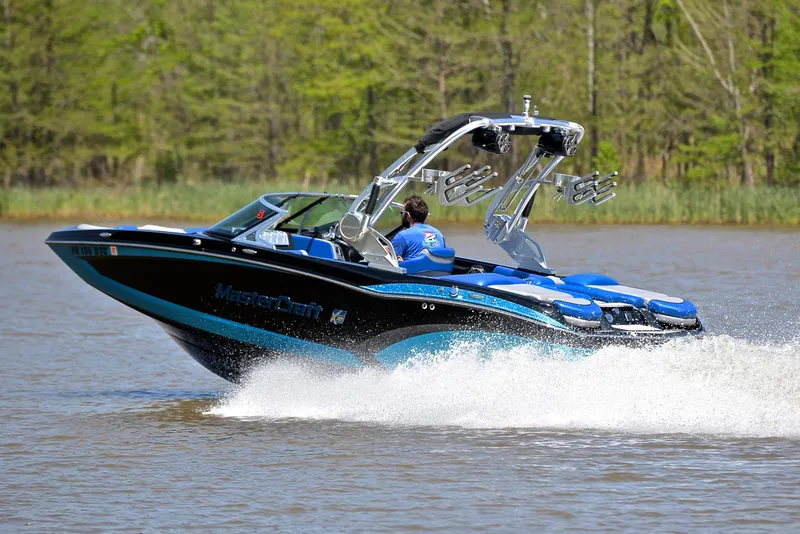 Slide: The Image of 2015 MasterCraft X20 boat cruising on a lake with lush green trees in the background. - 4