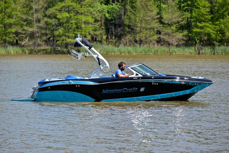 Slide: The Image of 2015 MasterCraft X20 boat cruising on a calm lake with lush green trees in the background. - 7