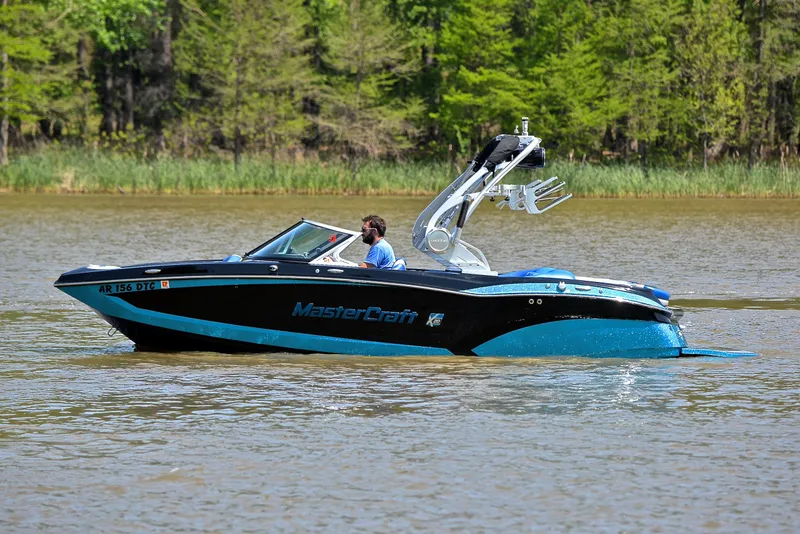 Slide: The Image of 2015 MasterCraft X20 boat cruising on a lake with lush green trees in the background. - 9