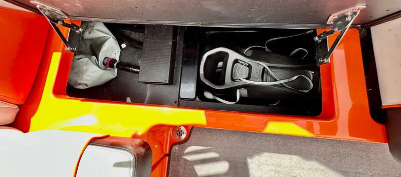 Slide: The Image of 2020 Malibu 21VLX boat storage compartment with orange trim and equipment. - 13