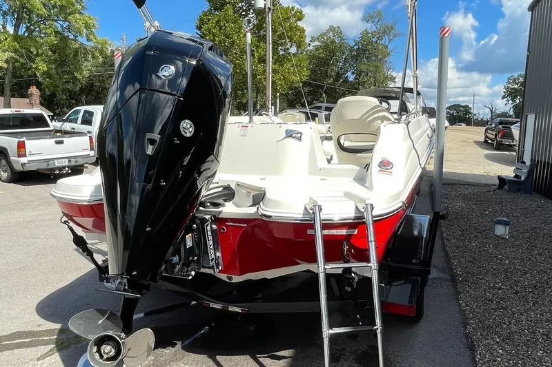 Slide: The Image of 2023 Stingray 212 SC boat with powerful outboard motor, red and white design, parked outdoors. - 2