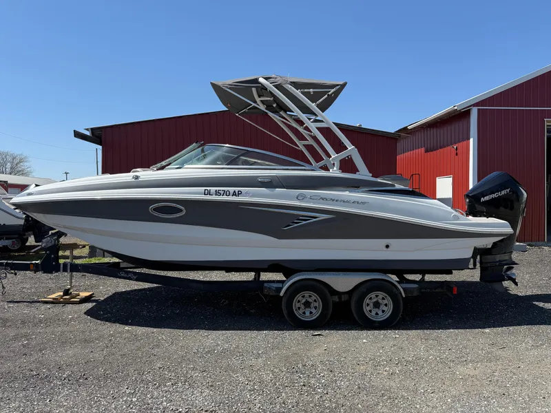 Slide: The Image of 2022 Crownline Eclipse E235 XS boat on trailer, parked near red building. - 2