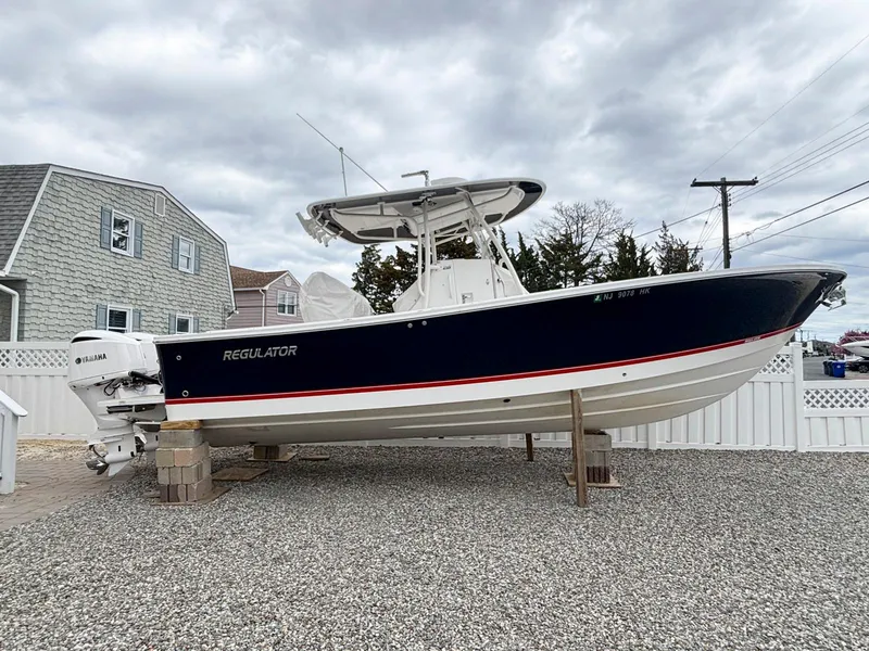 Slide: The Image of 2018 Regulator 28 boat on blocks, parked in a gravel driveway, overcast sky. - 0