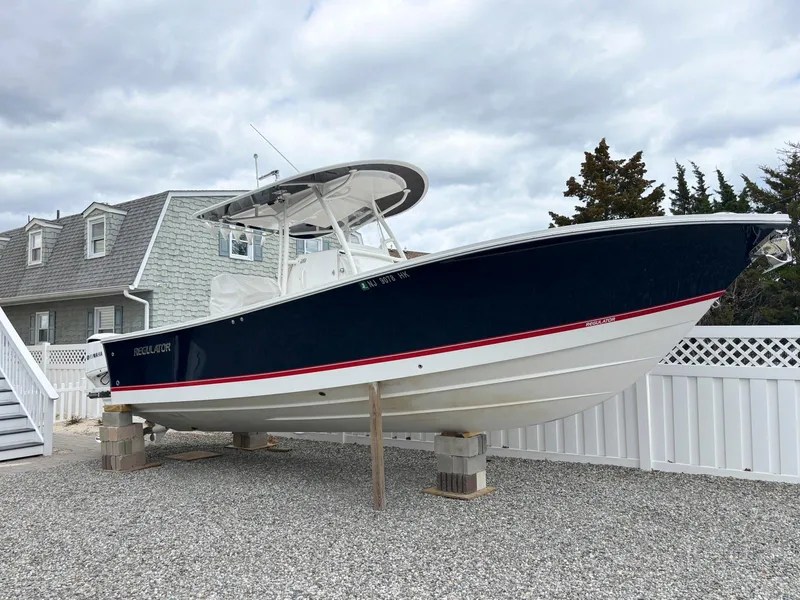 Slide: The Image of 2018 Regulator 28 boat on blocks, navy hull, white trim, near coastal home. - 1