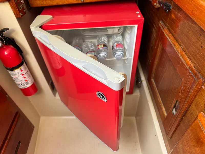 Slide: The Image of Red mini fridge with open door, stocked with water bottles, inside a 1985 Catalina 30 boat. - 12