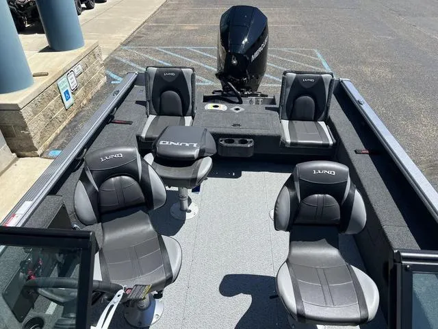 Slide: The Image of 2024 Lund 2025 Impact XS Sport boat interior with four seats and motor, parked on pavement. - 20