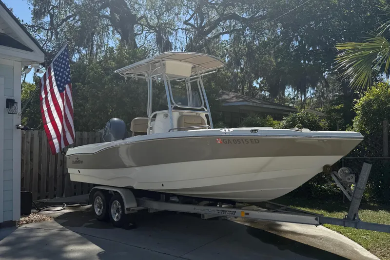 Slide: The Image of 2018 NauticStar 211 Hybrid boat on trailer with American flag in driveway. - 0